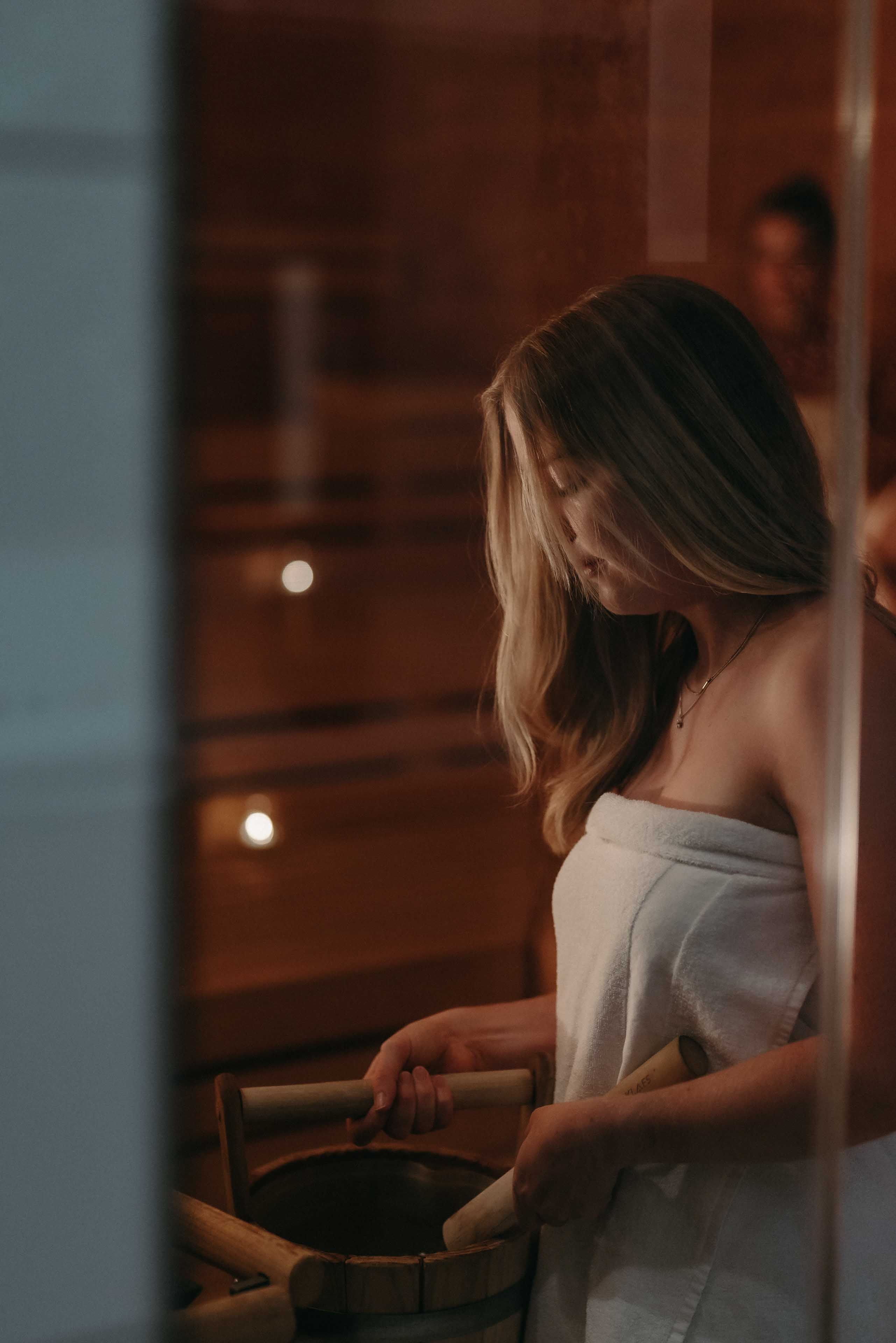 Women in the wooden sauna adds water to the hot stones