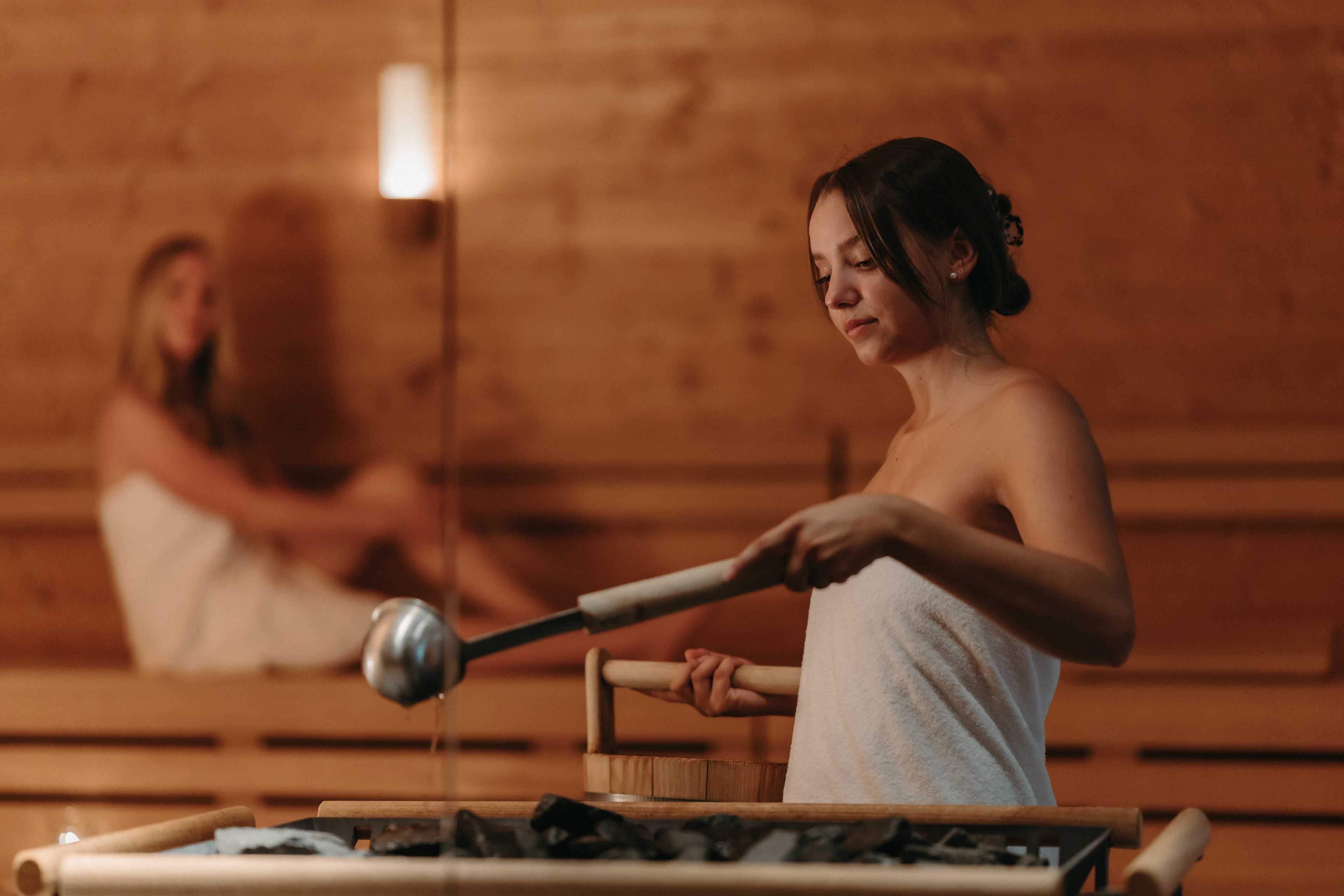 Women in the wooden sauna adds water to the hot stones wider shot