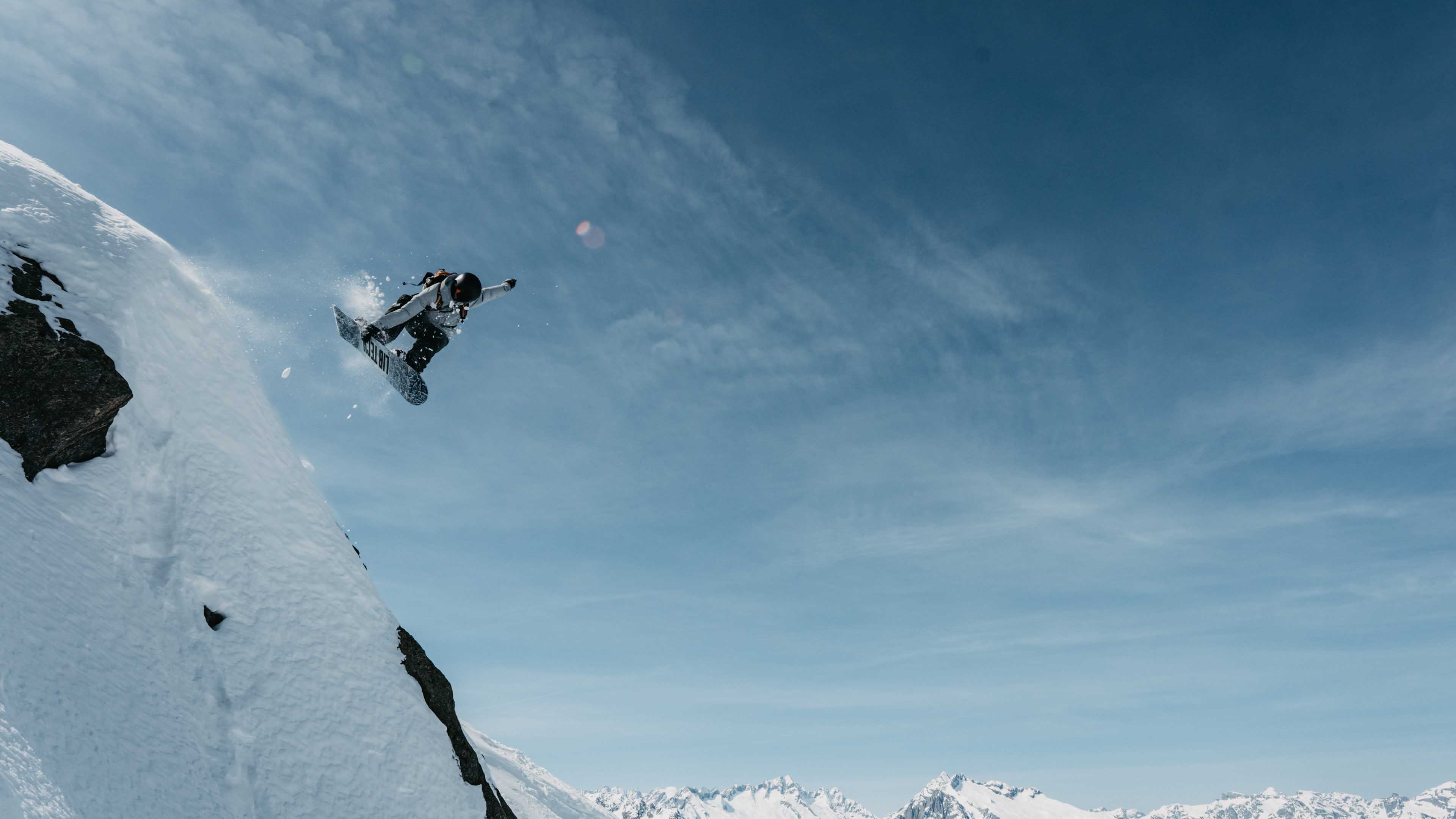 Snowboarder jumping off a cliff with a view of the Alps