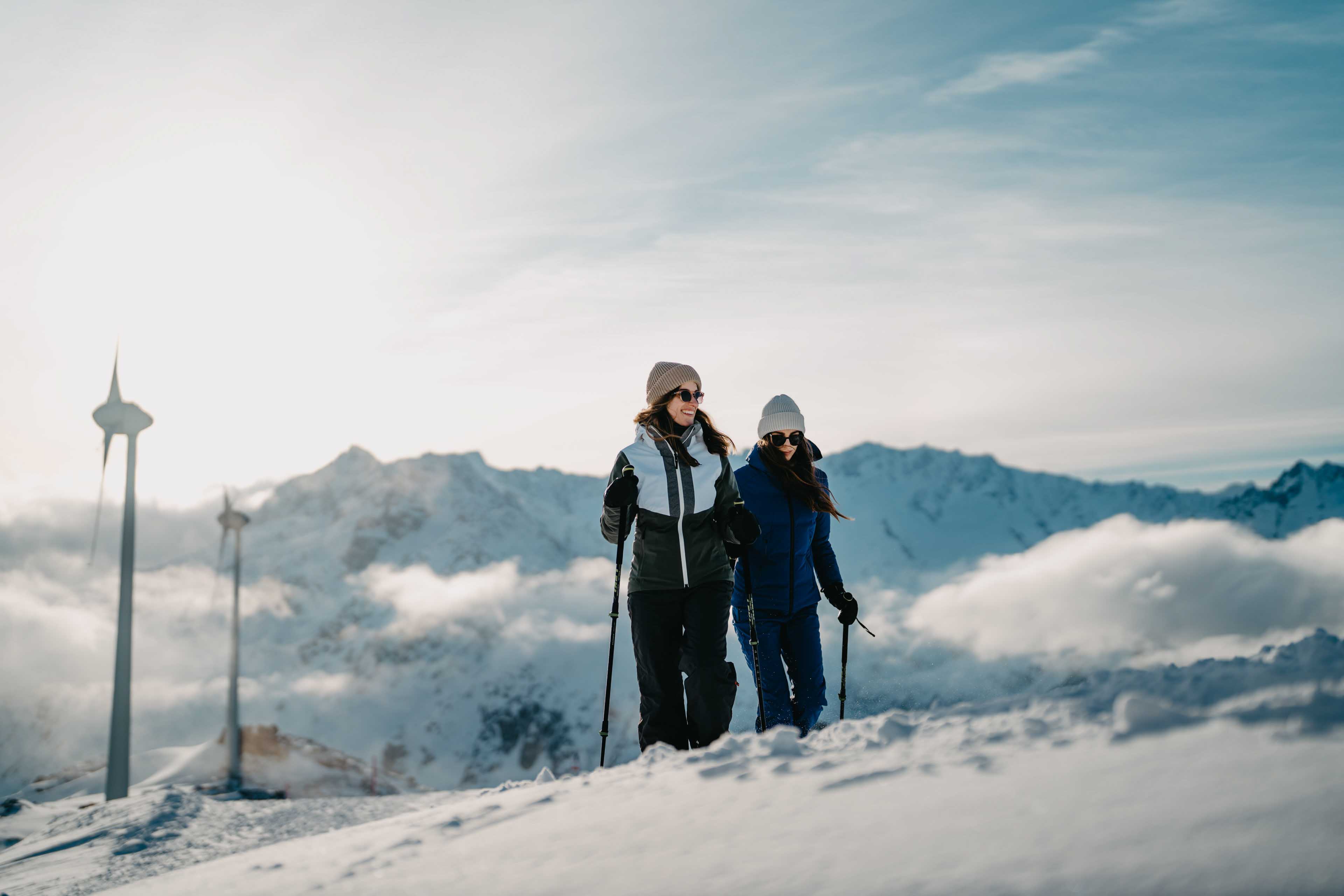 Two women snowshoeing in the Swiss alps. Wind turbines in the background, other perspective.